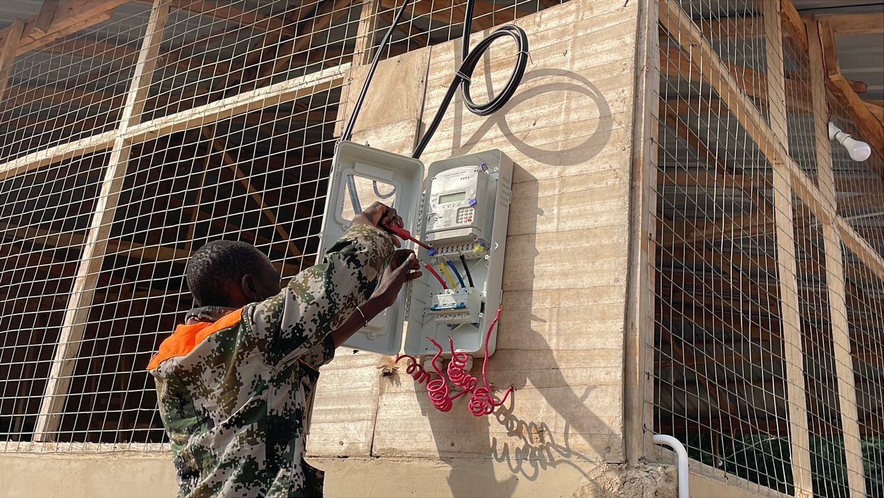 An electrician wiring the consumer unit and meter on an exterior wall.
