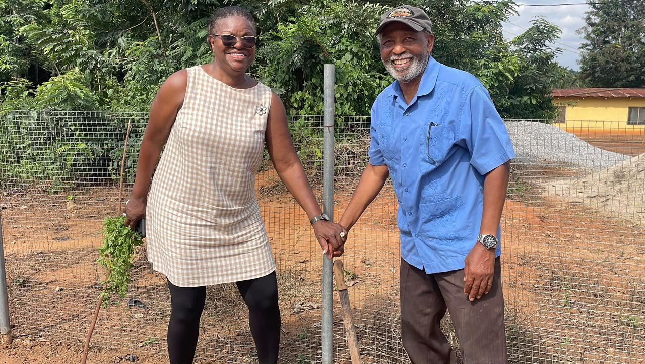 Founders Pastor and Mrs. Anthony at the factory site, cassava stems and a cutlass in hand.
