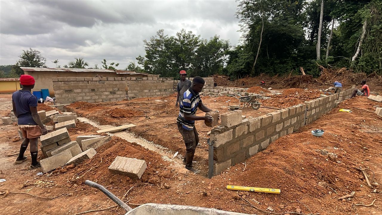 Masons laying concrete blocks on site, with a wheelbarrow and spirit level in the foreground.