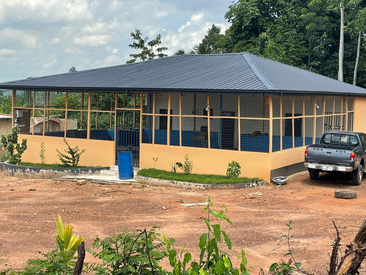 A finished outbuilding on site, painted with blue trim, with a vehicle parked beside it.