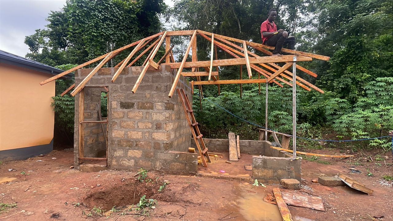A worker fixing timber roof trusses onto a small block structure on site.